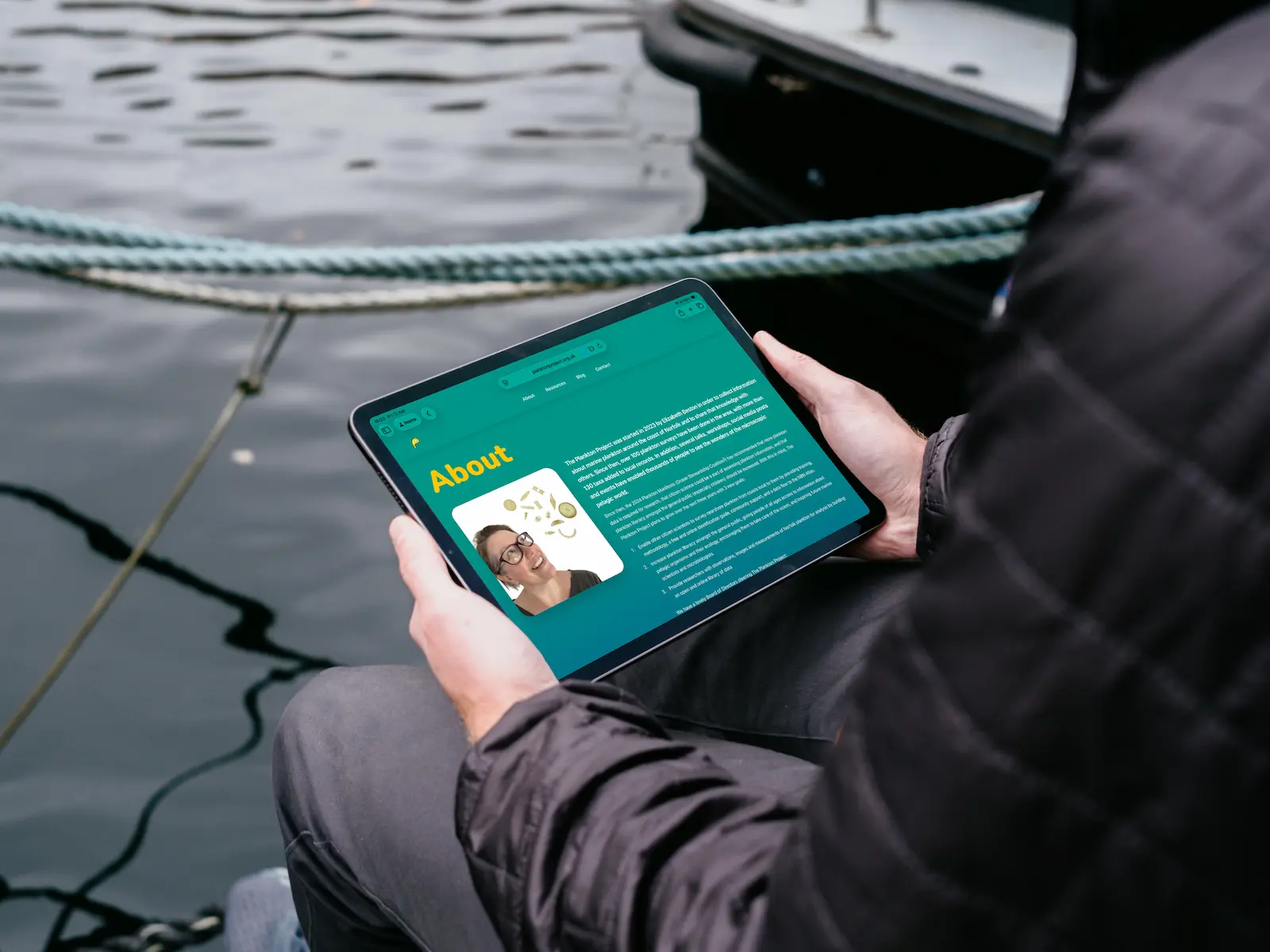 An image of the Plankton Project website on an iPad being held by a man sat by the water.